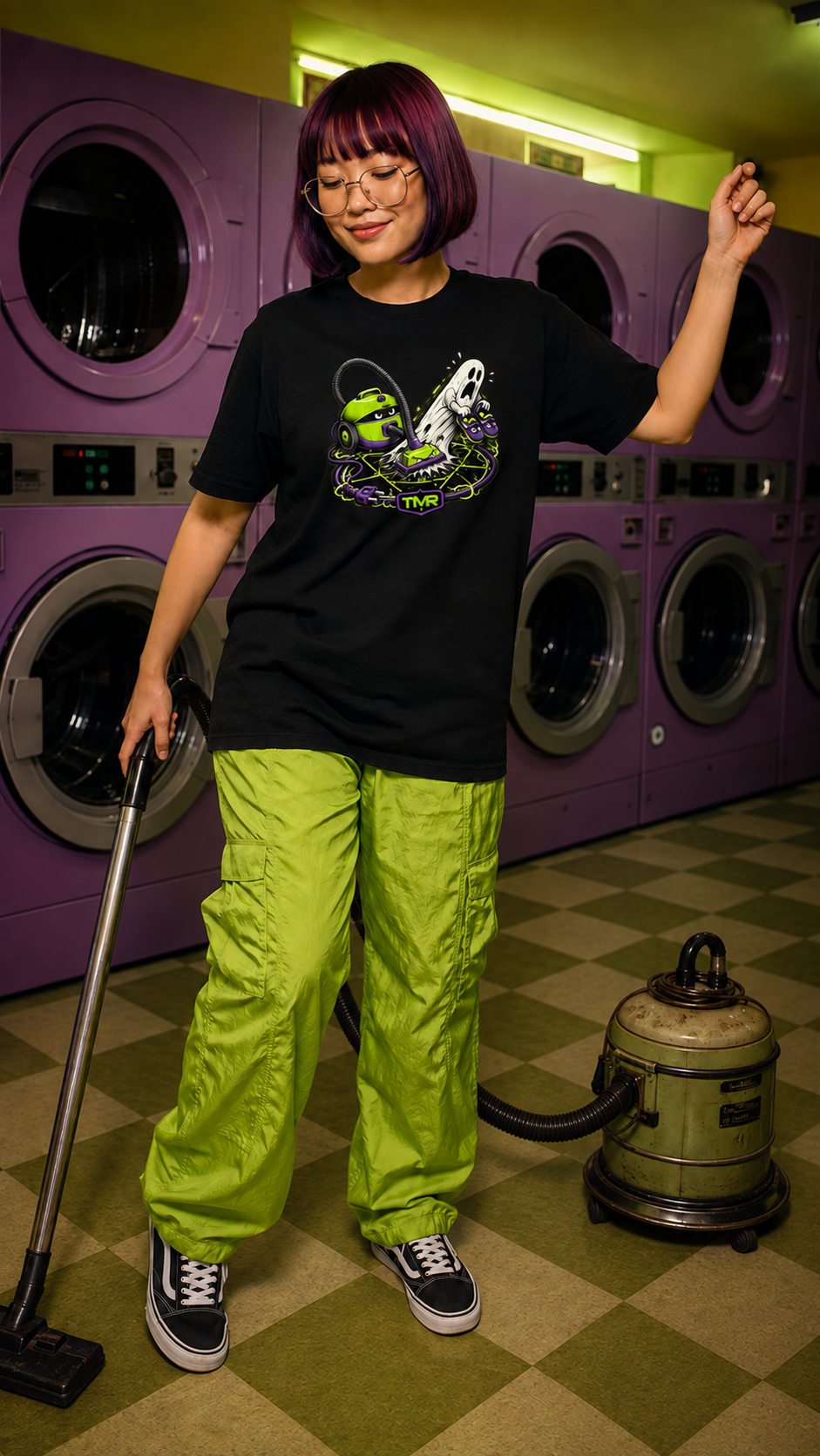 Cazafantasmas doméstico — Camiseta 3 Mockup digital de una modelo adulta con camiseta negra Cazafantasmas doméstico en una lavandería violeta; se ve el estampado frontal de una aspiradora lima, un fantasma blanco y el emblema TMR.