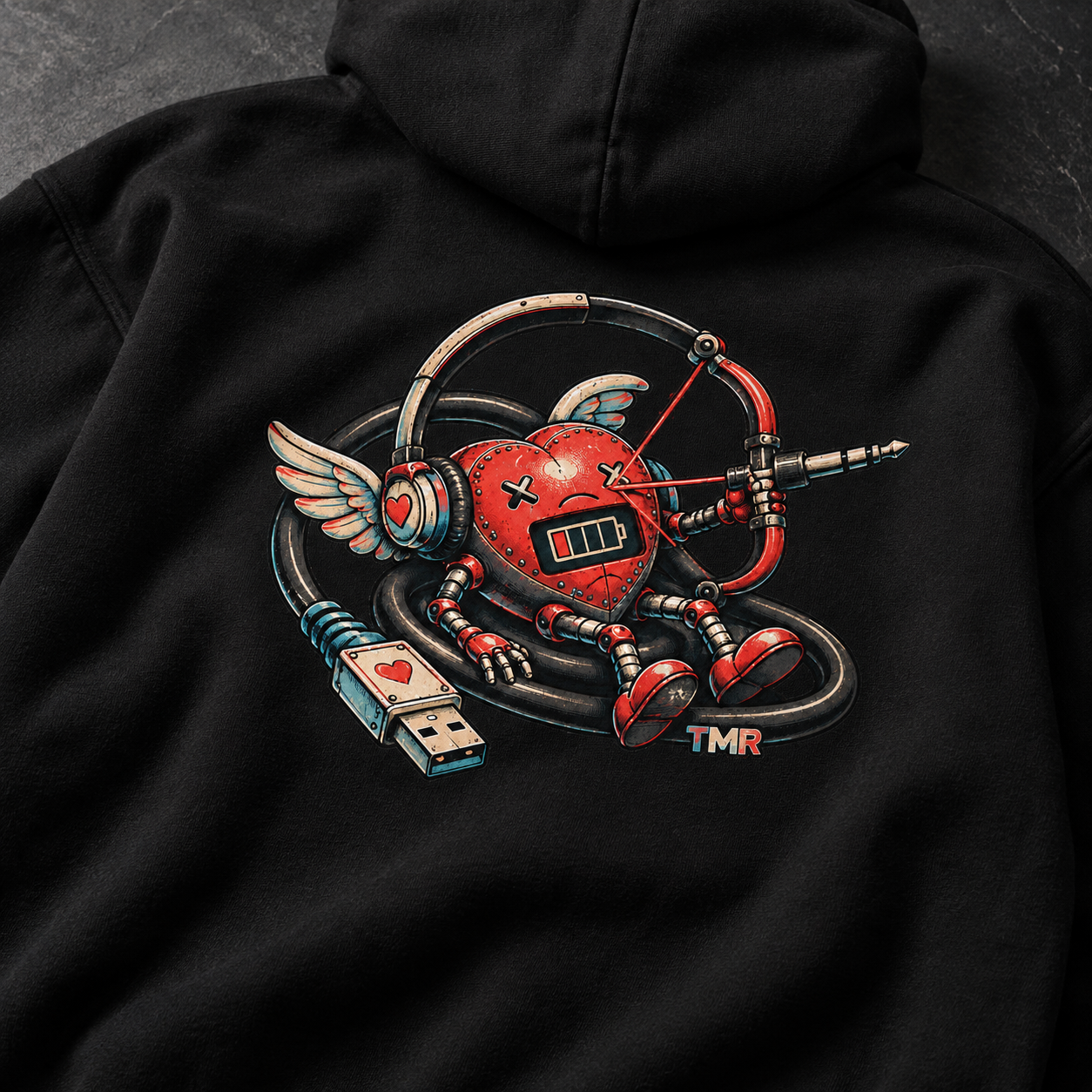 Cupido sin batería — Sudadera 3 Detalle del estampado Cupido sin batería TMR sobre tejido negro: corazón mecánico, indicador de batería, alas y cable USB.