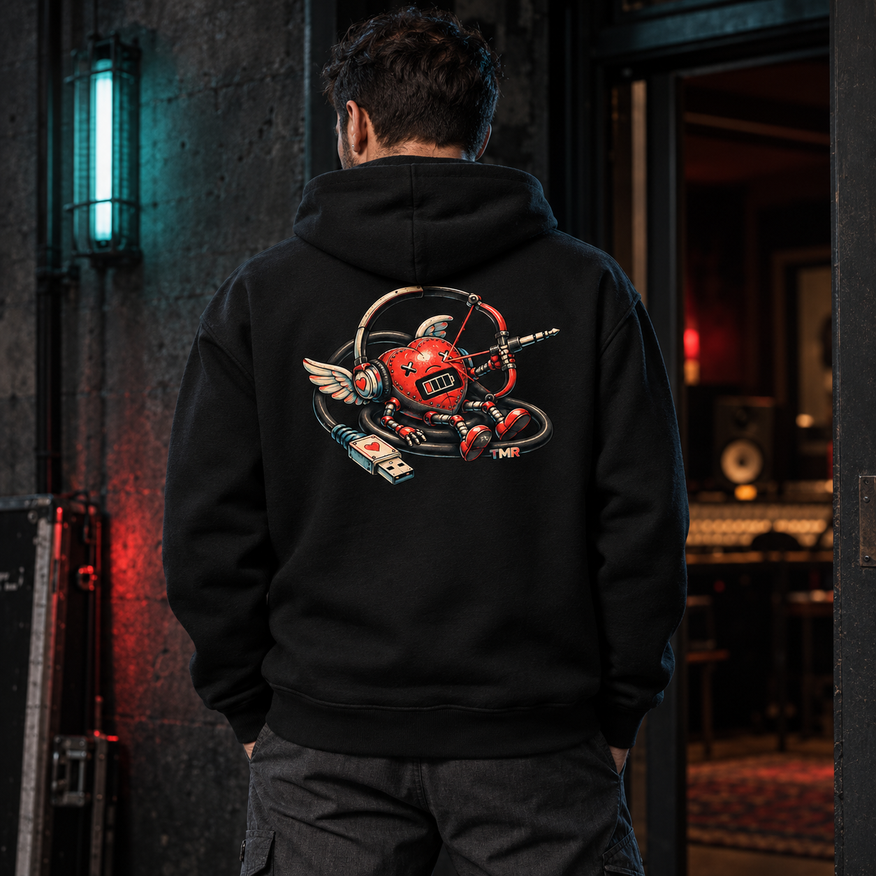 Cupido sin batería — Sudadera 1 Sudadera negra Cupido sin batería TMR en un modelo adulto de espaldas, con corazón mecánico, auriculares, alas y cable USB.