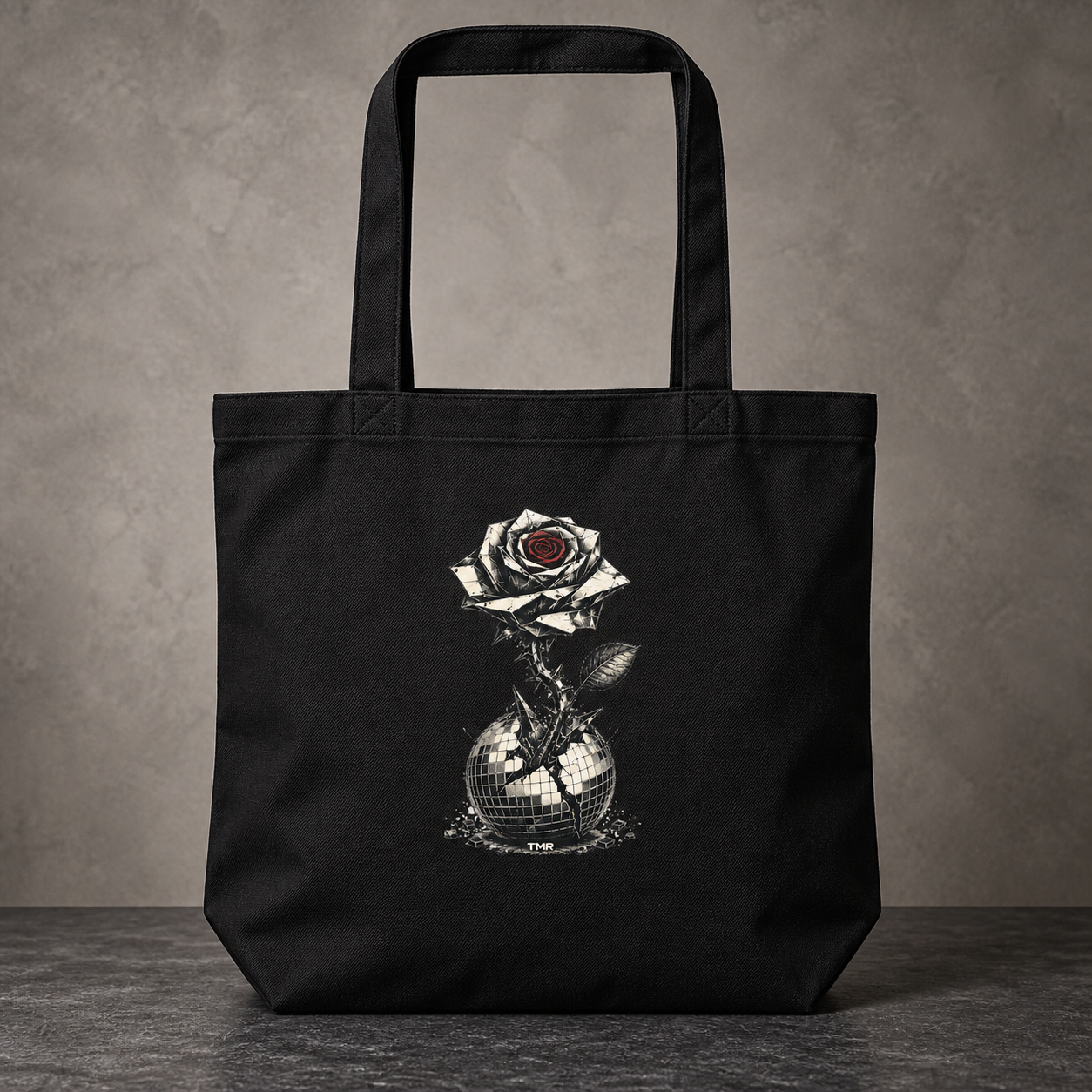 Flor blindada — Tote 1 Tote negra Flor blindada de TMR, vista frontal de estudio con asas completas y estampado centrado sobre algodón.