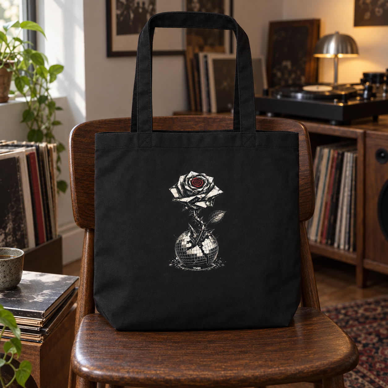 Flor blindada — Tote 2 Tote Flor blindada de TMR sobre una silla de madera junto a vinilos; vista del dibujo integrado en la tela negra.