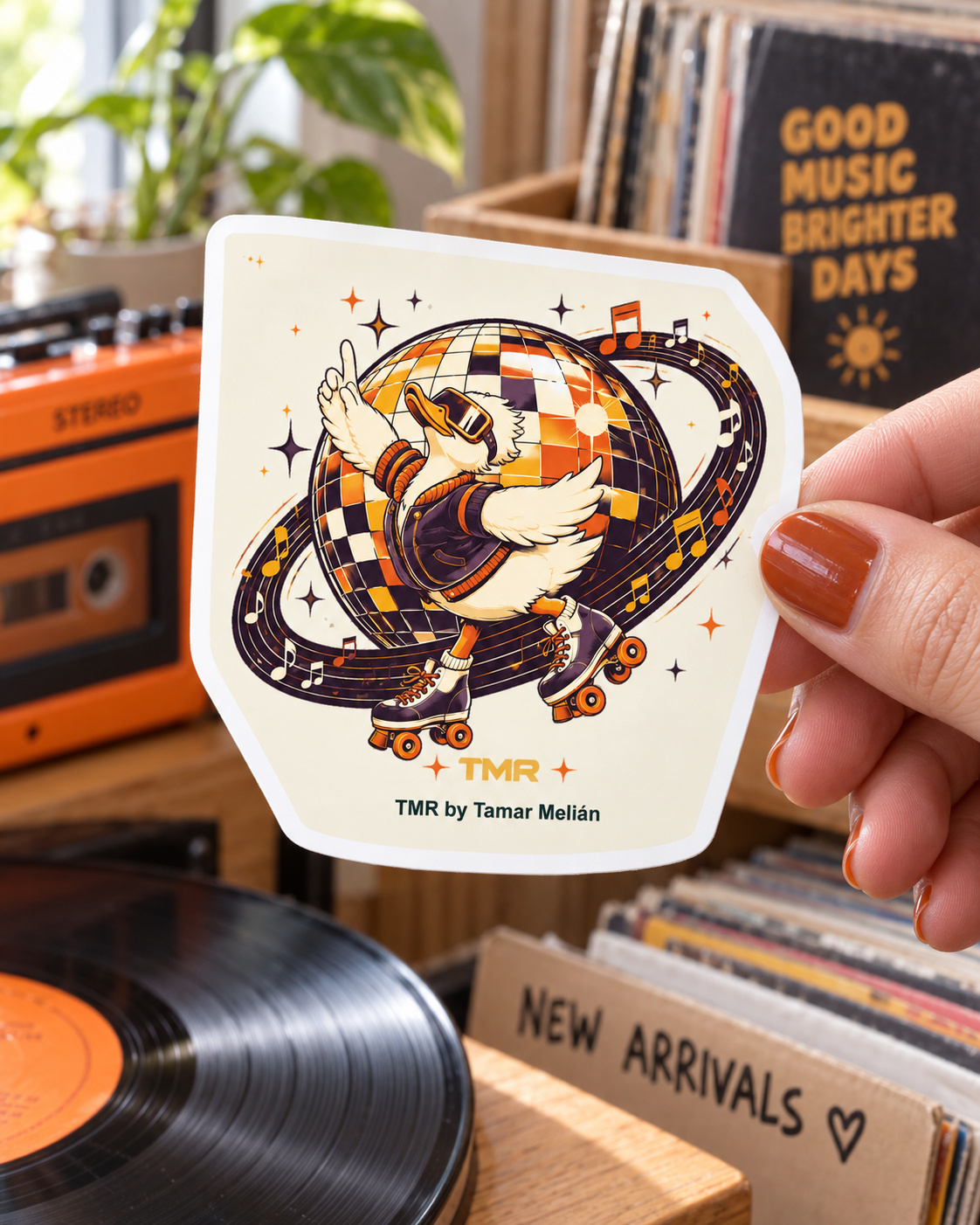 Pato en órbita — Pegatina 3 Una mano muestra la pegatina Pato en órbita de TMR junto a un radiocasete naranja y discos de vinilo.