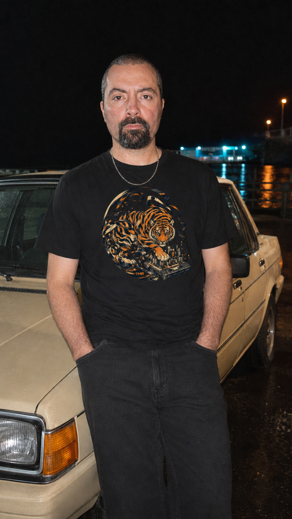 Tigre radiocasete — Camiseta Classic 2 Retrato digital basado en referencias autorizadas de Tamar Melián mostrando el estampado frontal de Tigre radiocasete en una camiseta negra, junto a un coche beige de noche.