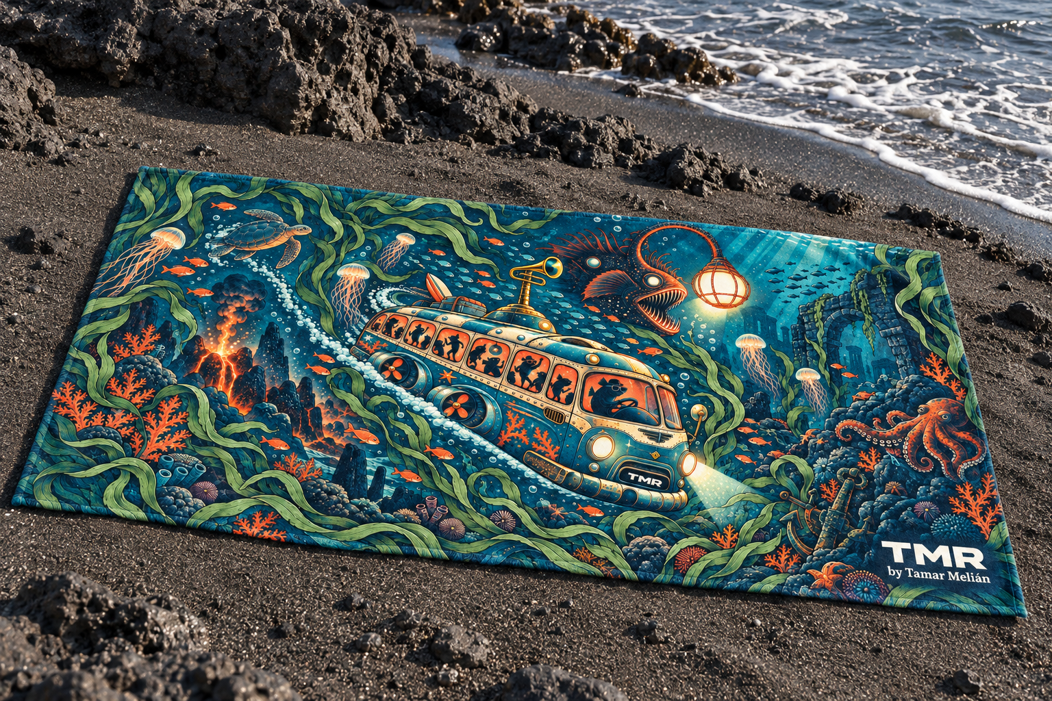 Guagua abisal — ビーチタオル 76 × 152 cm 3 Mockup digital de la toalla Guagua abisal sobre arena negra junto a rocas volcánicas y el mar, con la guagua submarina y la firma TMR by Tamar Melián.